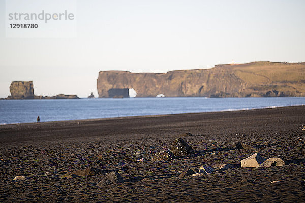 Schwarzer Sand am Strand von Reynisfjara mit einem natürlichen Bogen im Hintergrund  Island