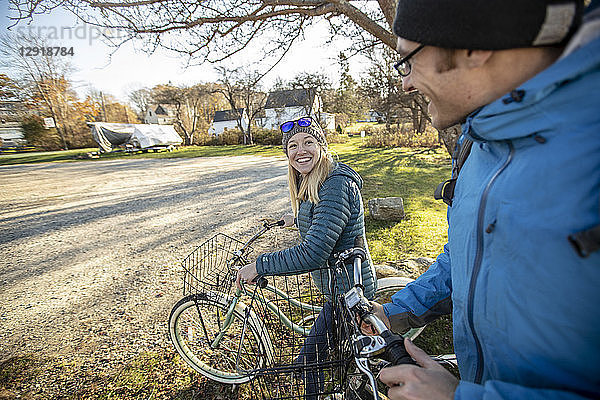 Lächelndes junges Paar beim Spaziergang mit Fahrrädern durch ein Dorf im Herbst  Portland  Maine  USA