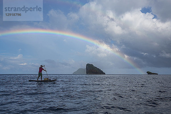 Seitenansicht eines Mannes beim Paddeln im Meer unter einem Regenbogen  Misool  Raja Ampat  Indonesien