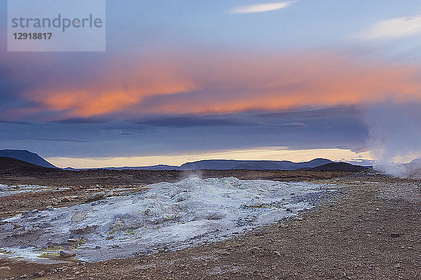 Ein blau gefärbtes  kochend heißes Schlammbecken stößt Dampf aus  während der Sonnenuntergang den Himmel orange färbt  im Hverarˆšˆ'ndor Hverir Geothermalgebiet am Namaskard-Pass  Nordisland.