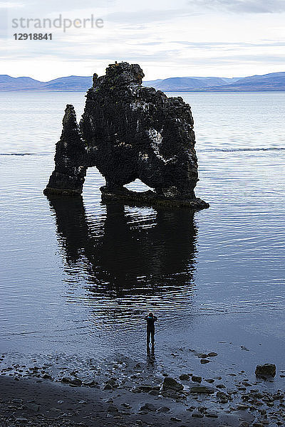 Silhouette einer Wanderin  die an der Küste steht und eine Felsformation betrachtet  Hvitserkur  Island