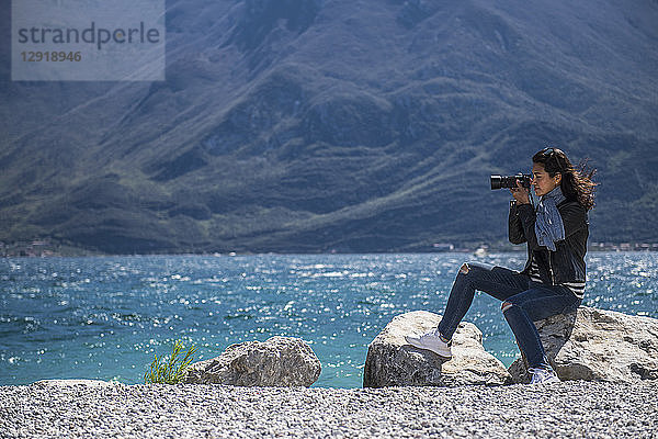 Frau sitzt auf einem Felsen an der Küste und fotografiert den Gardasee  Verona  Italien