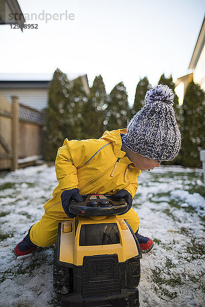 Vorderansicht eines Kleinkindes  das im Winter im Garten mit einem Spielzeugauto fährt