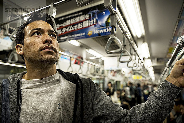 Mann steht in einem U-Bahn-Wagen voller Menschen  Tokio  Japan