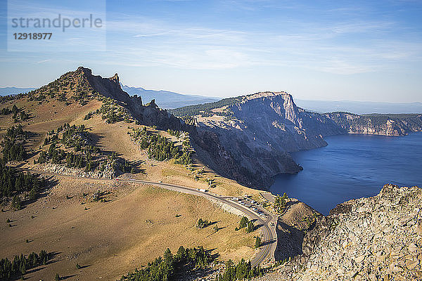 Blick auf eine Bergstraße  die sich entlang eines exponierten Bergrückens über einem tiefblauen See schlängelt  Crater Lake  Oregon  USA