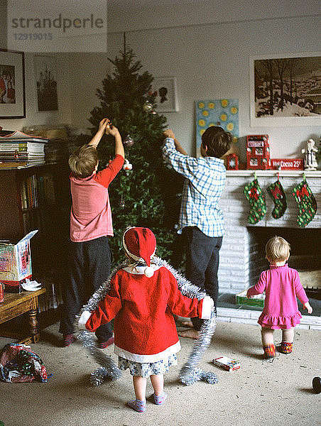 Rückansicht einer Gruppe von vier Kindern beim Schmücken des Weihnachtsbaums