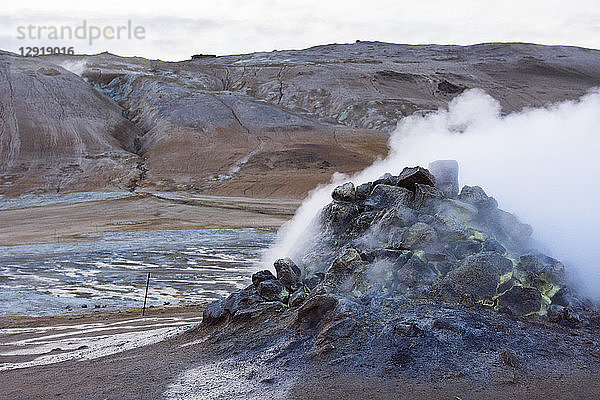 Eine aktive Dampfquelle spuckt Schwefel und andere giftige Gase in Form von Dämpfen aus  die den Boden in der Umgebung blau und leuchtend gelb gefärbt haben. Im Hintergrund ist der Berg Namafjall im Hverarˆšˆ'ndor Hverir Geothermalgebiet am Namaskard-Pass in Nordisland zu sehen.