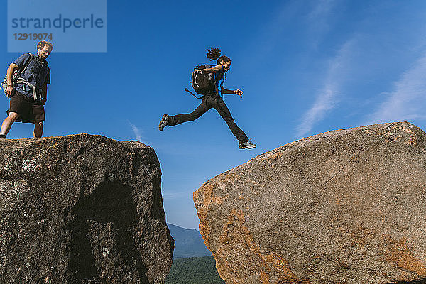 Seitenansicht einer Frau  die beim Wandern über einen Felsblock springt  Pitchoffâ€ Mountain  Adirondack Mountains  New York State  USA