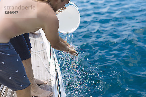 Seitenansicht eines Mannes beim Händewaschen mit Wasser aus einem Eimer auf einem Segelboot