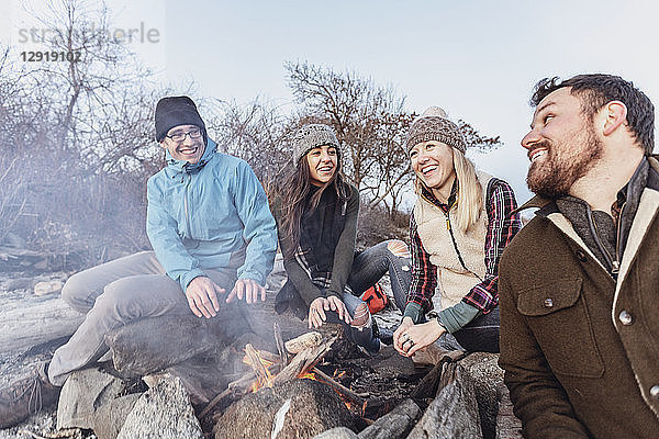 Vier erwachsene Freunde wärmen sich am Lagerfeuer  während sie an einem felsigen Küstenstrand im Herbst zelten  Portland  Maine  USA
