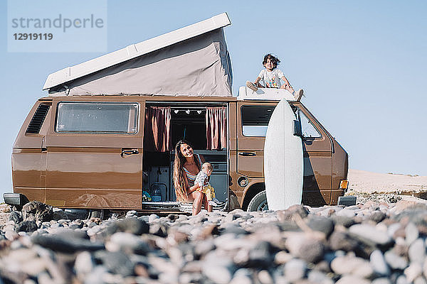Zurückgezogene Ansicht einer jungen Familie  die an einem alten Wohnmobil am kopfsteingepflasterten Strand sitzt  Teneriffa  Kanarische Inseln  Spanien