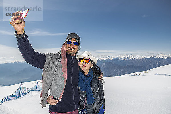 Älteres Paar  das sich umarmt  während es ein Selfie auf einem schneebedeckten Berggipfel macht  Malcesine  Verona  Italien