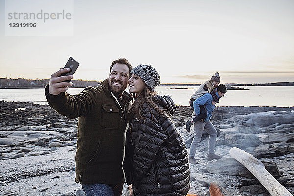 Erwachsenes Paar macht ein Selfie vor einem Lagerfeuer mit Freunden im Hintergrund  Portland  Maine  USA