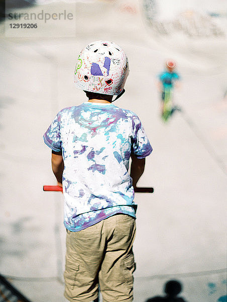 Rückansicht eines Jungen mit Tretroller in einem Skateboard-Park