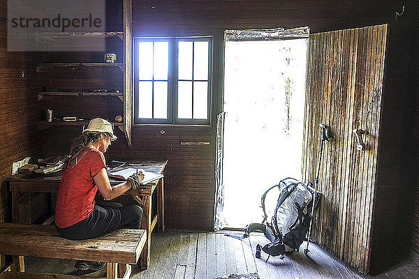Ein Wanderer macht eine Pause an Theodore Roosevelts Cabin auf dem Muav Saddle  weit draußen am North Rim des Grand Canyon  und unterschreibt ein historisches Wanderregister  Arizona  USA