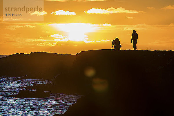 Silhouettenansicht von zwei Fotografen  die den Sonnenuntergang auf der südlichen Halbinsel Reykjanes einfangen  Reykjanes  Island