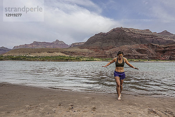 Junge Frau taucht aus dem kalten Wasser des Colorado River auf  nachdem sie ihre Füße abgekühlt hat  um das Ende eines langen Wandertages zu feiern  Grand Canyon  Arizona  USA