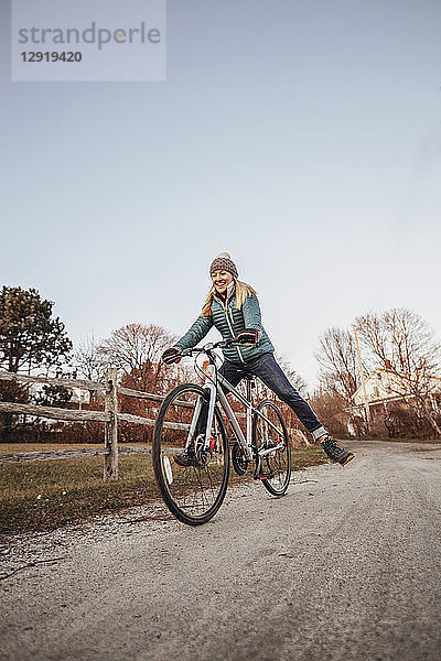Junge Frau fährt mit dem Fahrrad auf einer unbefestigten Straße neben einem Holzzaun  Portland  Maine  USA