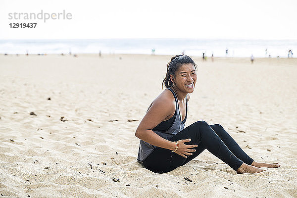 Glückliche Sportlerin sitzt am Sandstrand bei Tageslicht  Oahu  Hawaii  USA