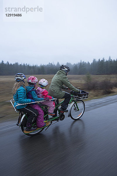 Mutter fährt mit ihren drei Mädchen auf dem Fahrrad von zu Hause zur Schule im Regen  Sandpoint  Idaho  USA