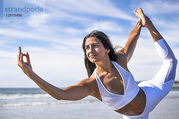 Foto einer jungen Frau  die auf einem Bein steht  während sie am Strand Yoga macht
