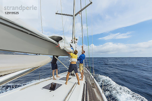 Eine Gruppe von drei Männern ist mit der Vorbereitung der Segelausrüstung beschäftigt.