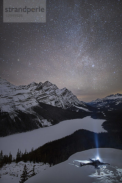 Mann mit Stirnlampe im Schnee liegend in der Nähe des Peyto Lake bei Nacht  Banff National Park  Alberta  Kanada