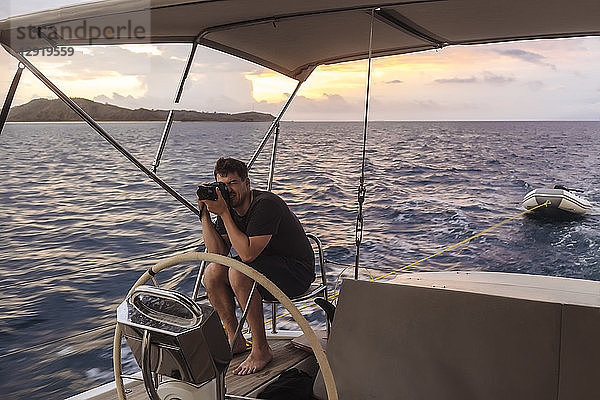 Totale Aufnahme eines jungen Mannes mit Kamera auf einem Segelboot bei Sonnenuntergang