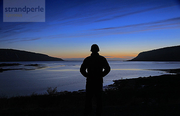 Silhouette eines Mannes  der einen schönen Sonnenuntergang über einem Fjord genießt  Westfjorde  Island