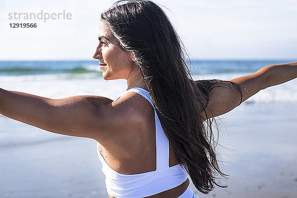 Rückansicht einer jungen Frau mit schwarzen Haaren beim Yoga am Strand