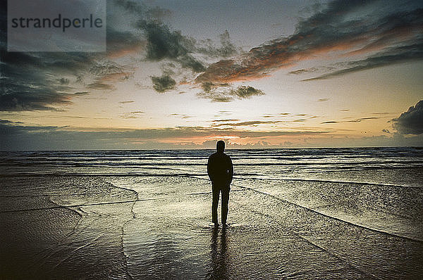 Ein Mann steht am Strand und beobachtet die Wellen und den Sonnenuntergang über dem Pazifischen Ozean  Oregon  USA