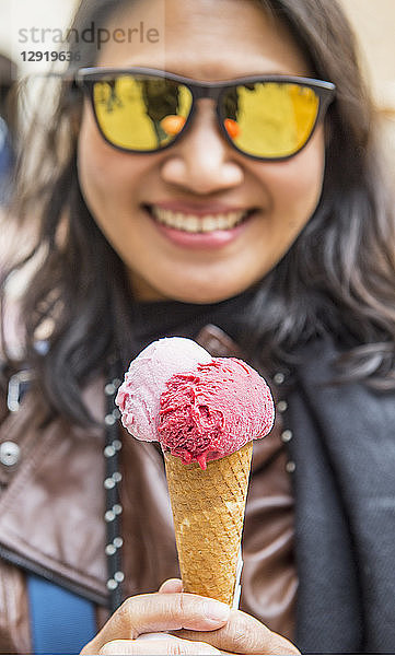 Porträt einer Frau mit Sonnenbrille  die lächelnd ein Eis in der Hand hält  Florenz  Toskana  Italien