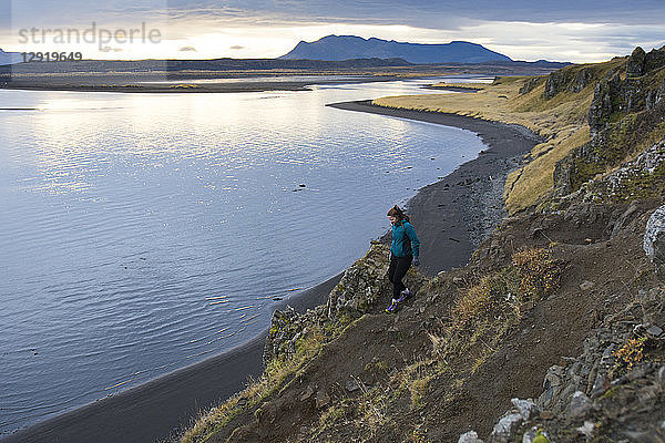 Wanderin beim Abstieg von einem Küstenfelsen und beim Gehen in Richtung Meeresküste  Hvitserkur  Island