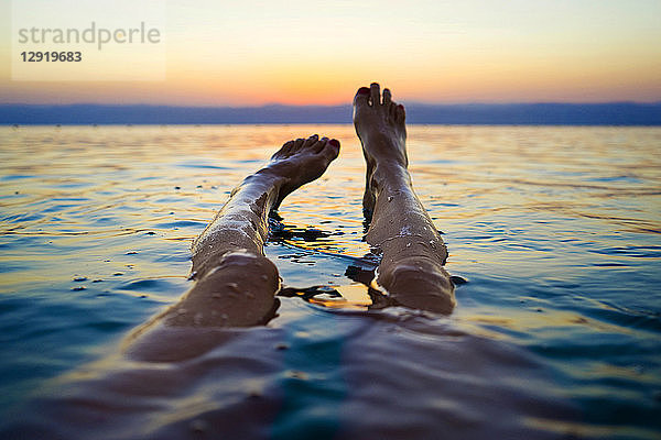 Persönliche Perspektive  aufgenommen mit den Beinen einer Frau  die bei Sonnenuntergang im Toten Meer schwimmt  Bezirk Madaba  Jordanien