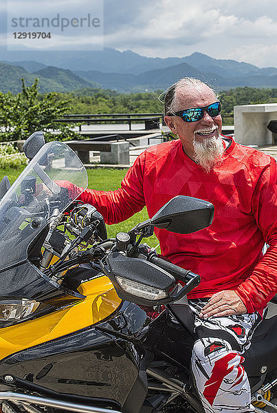 Lächelnder älterer Mann mit Bart auf einem Motorrad sitzend  Nan  Mueang Chiang Rai District  Thailand