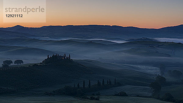 Vor der Morgendämmerung liegt Nebel in den Feldern und Hügeln des Val d'Orcia hinter einem Bauernhaus auf einem kleinen Felsvorsprung  UNESCO-Weltkulturerbe  Toskana  Italien  Europa