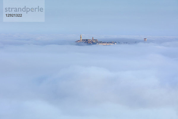 Der Uhrturm und der Glockenturm der Kathedrale von Pienza erheben sich über den Wolken und dem Nebel  der das darunter liegende Val d'Orcia bedeckt  UNESCO-Weltkulturerbe  Toskana  Italien  Europa