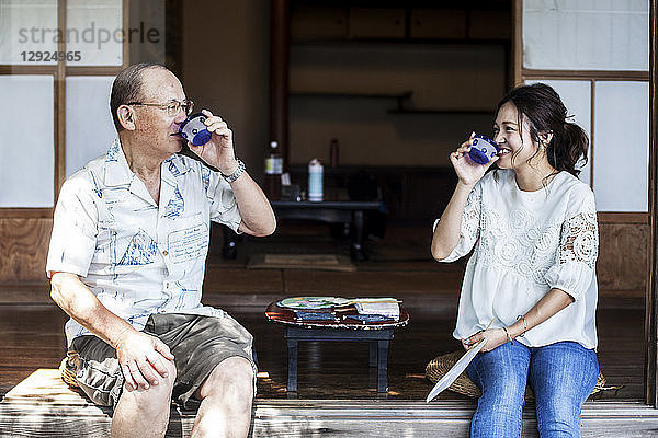 Japanischer Mann und Frau sitzen auf dem Boden auf der Veranda eines traditionellen japanischen Hauses und trinken Tee.