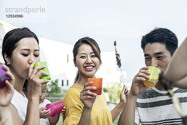 Gruppe von japanischen Männern und Frauen  die im Freien stehen und aus Plastikbechern trinken.