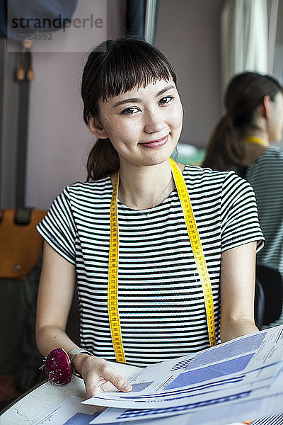Japanische Modedesignerin  die in ihrem Atelier arbeitet und in die Kamera lächelt.
