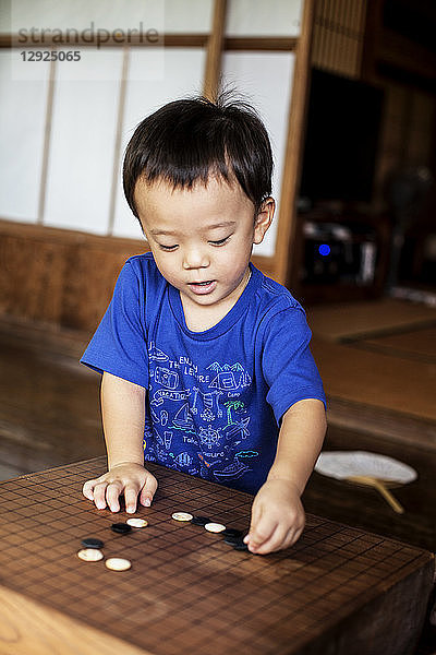 Kleiner Junge steht auf der Veranda eines traditionellen japanischen Hauses und spielt Go.