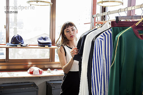 Japanische Verkäuferin steht im Bekleidungsgeschäft und schaut auf ein Hemd.