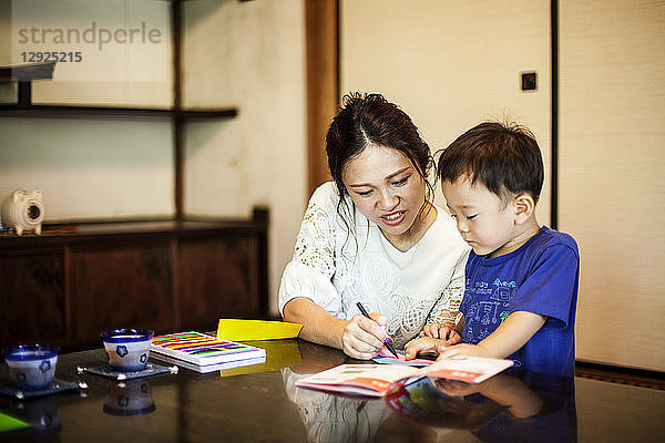 Japanische Frau und kleiner Junge sitzen an einem Tisch und malen mit Farbstiften.