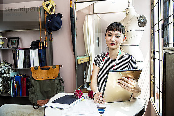 Japanische Modedesignerin  die in ihrem Atelier arbeitet und in die Kamera lächelt.