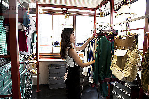 Japanische Verkäuferin  die in einem Bekleidungsgeschäft steht und Kleider auf einer Schiene arrangiert.