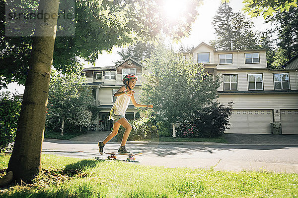 Tween Girl skatet auf dem Skateboard auf dem Bürgersteig in einem Wohnviertel