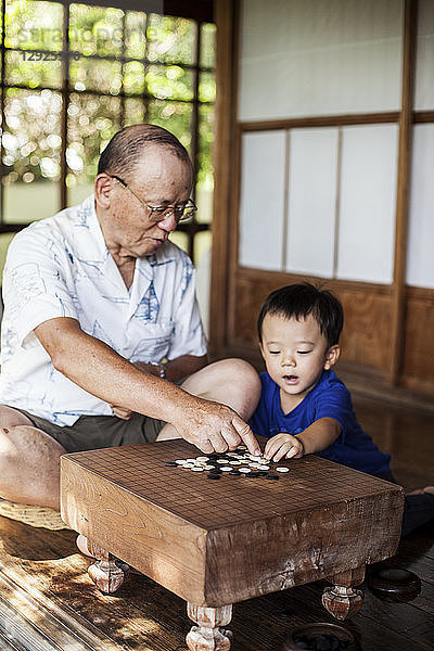 Japanischer Mann und kleiner Junge sitzen auf dem Boden auf der Veranda eines traditionellen japanischen Hauses und spielen Go.