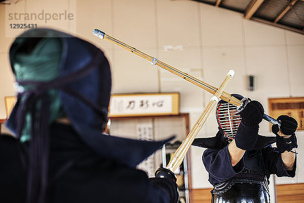 Zwei japanische Kendo-Kämpfer mit Kendo-Masken beim Üben mit dem Holzschwert in der Turnhalle.