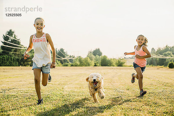 Mädchen rennen mit Labradoodle-Welpe durchs Feld