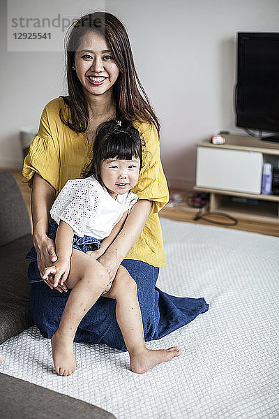 Porträt einer auf dem Boden sitzenden Japanerin mit einem jungen Mädchen auf dem Schoß  das in die Kamera lächelt.